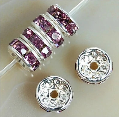 A string of pink crystal rondelle spacer beads threaded onto a silver wire, next to two loose beads.