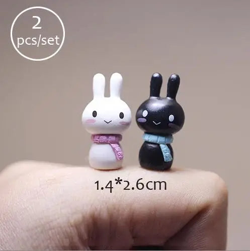 Two small white and black animal figurines are shown resting on a person's finger.