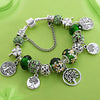 A silver charm bracelet featuring green leaf and floral accents, including a Tree of Life pendant.