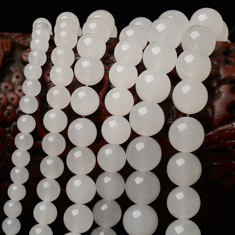 A close-up of natural white crystal quartz round beads arranged in a string for jewelry making.
