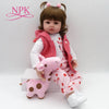 A lifelike reborn toddler doll with soft body and a pink outfit sitting on a white box.