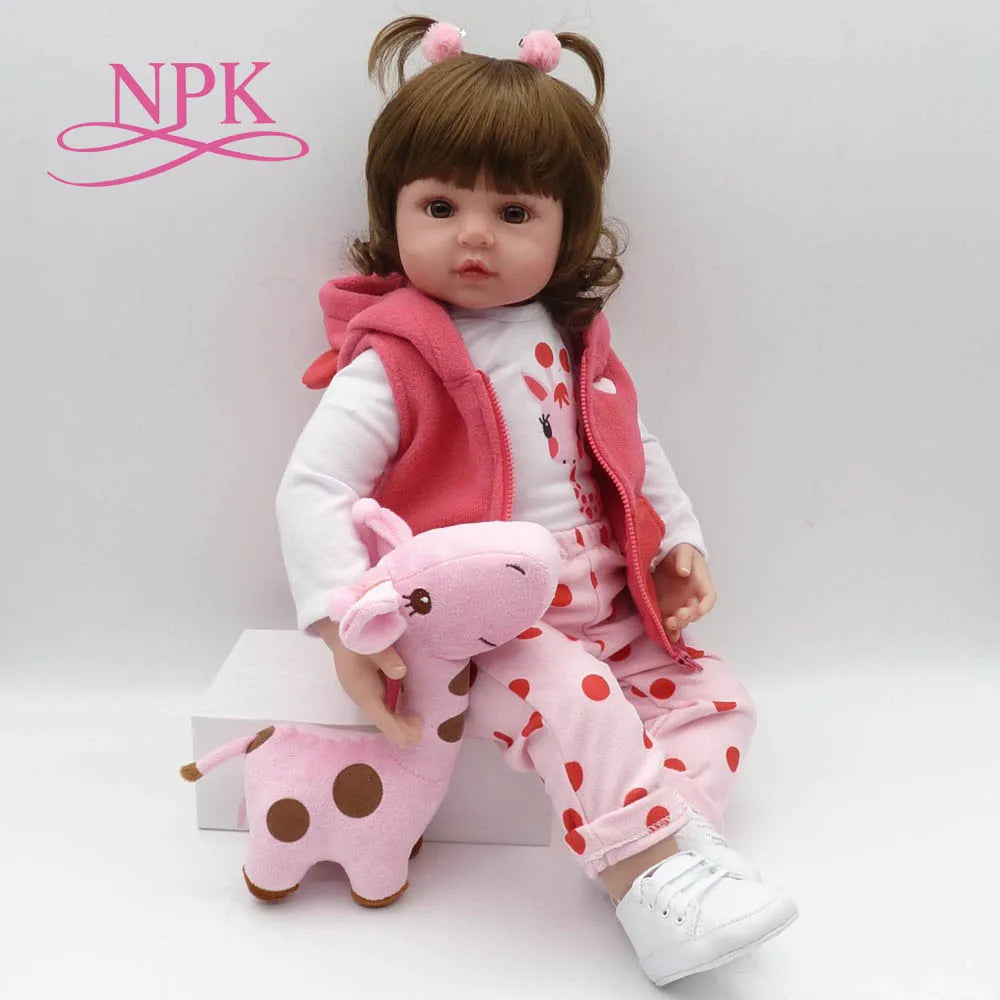 A lifelike reborn toddler doll with soft body and a pink outfit sitting on a white box.