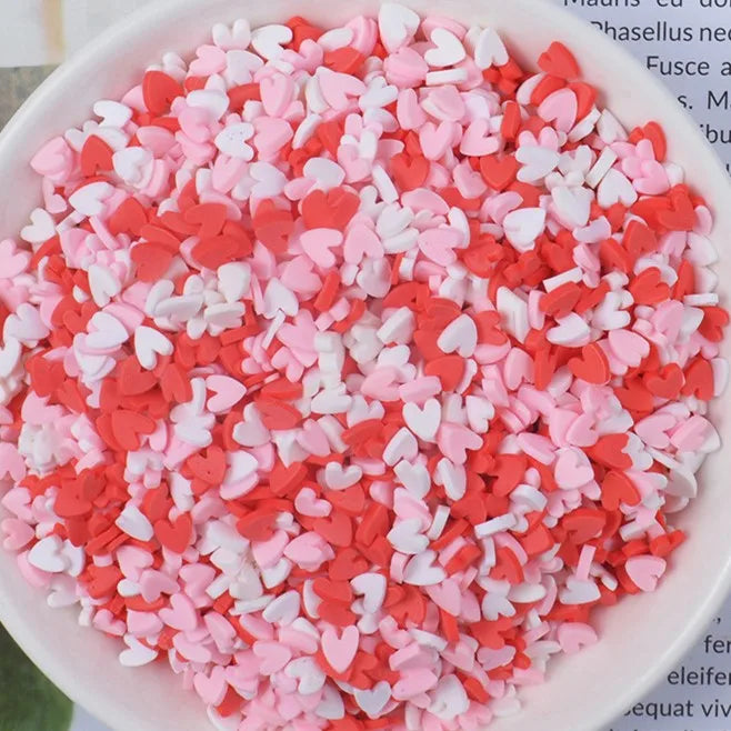 A bowl filled with heart-shaped fake candy sprinkles in shades of pink and red for slime and craft decorations.