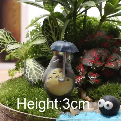A small, gray animal figurine with a yellow face is nestled in green moss and foliage.