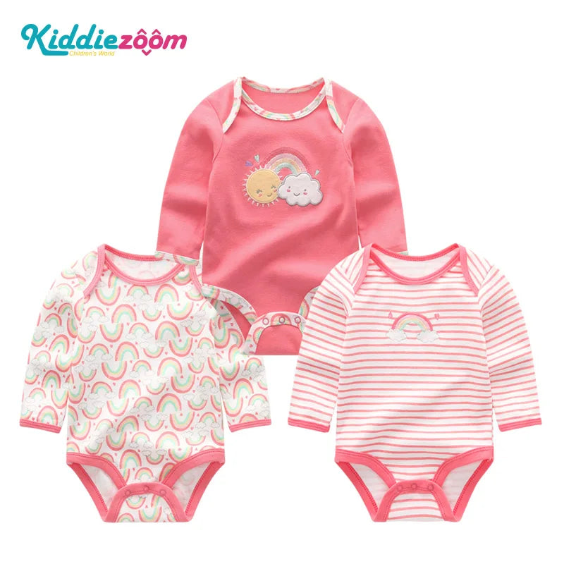 A set of three pink cotton baby bodysuits with long sleeves featuring colorful rainbow designs.
