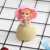 A small doll with bright orange hair and a pink bonnet wearing a purple dress, displayed on a grid background.