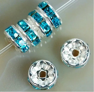 A string of blue crystal rondelle spacer beads threaded onto a clear wire, with loose beads nearby.