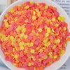 A bowl filled with heart-shaped fake candy sprinkles in shades of orange, pink, and yellow for slime and craft decorations.