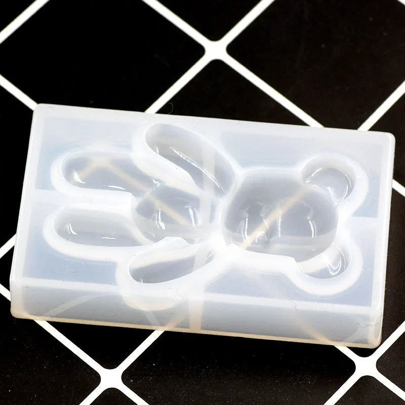 A white silicone mold shaped like a bear paw print for resin jewelry and crafts, resting on a black grid background.