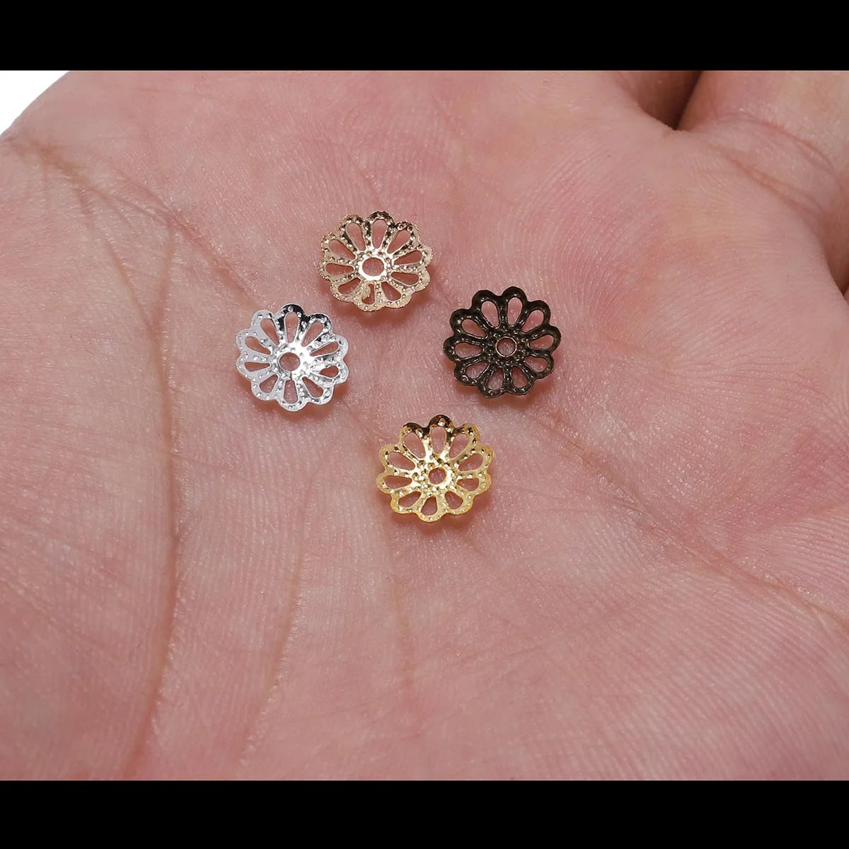 Three flower petal bead caps in gold, silver, and black are displayed on a hand.