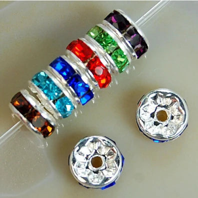 A string of colorful crystal rondelle spacer beads in various gemstone colors, alongside two silver metal findings.
