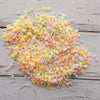 A pile of heart-shaped fake candy sprinkles in various pastel colors like pink, yellow, and blue on a wooden surface.
