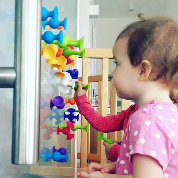 A young child is interacting with colorful Pop Little Sucker Building Blocks for Kids inside a wooden frame.