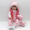 A toddler doll wearing a pink outfit and a matching pink headband, sitting on a white surface.