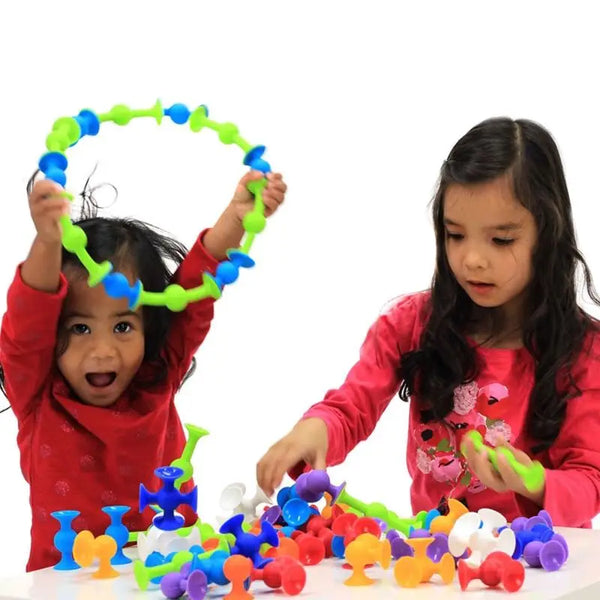 A young girl is playing with colorful Pop Little Sucker building blocks on a white surface.