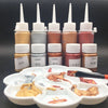 A row of glass bottles containing metallic gold acrylic paint in various shades and a set of paint palettes.