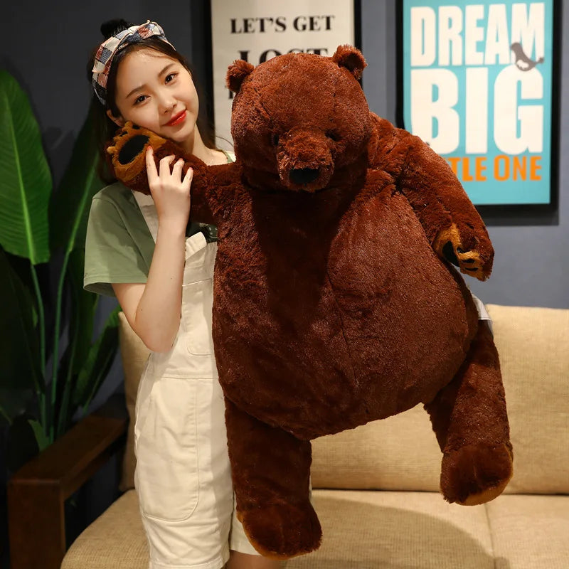 A young woman is posing with an oversized lifelike brown bear plush cushion.