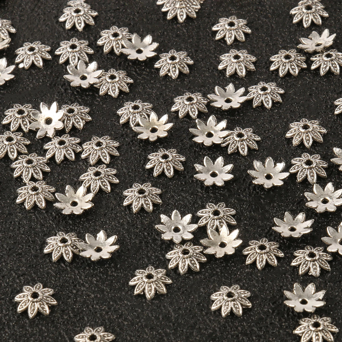 Silver Tibetan style hollow flower bead caps for jewelry making scattered on a dark surface
