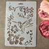A white stencil with floral and bird designs is shown next to pink and magenta rose petals.
