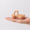 A small wooden car teether toy is held in an open human hand.