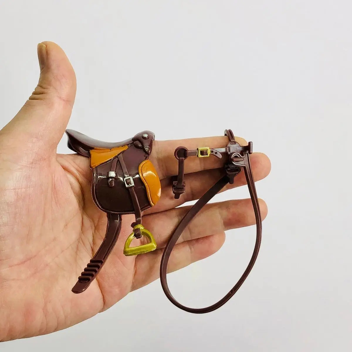 A brown leather horse saddle and riding prop accessory is held in a person's hand.
