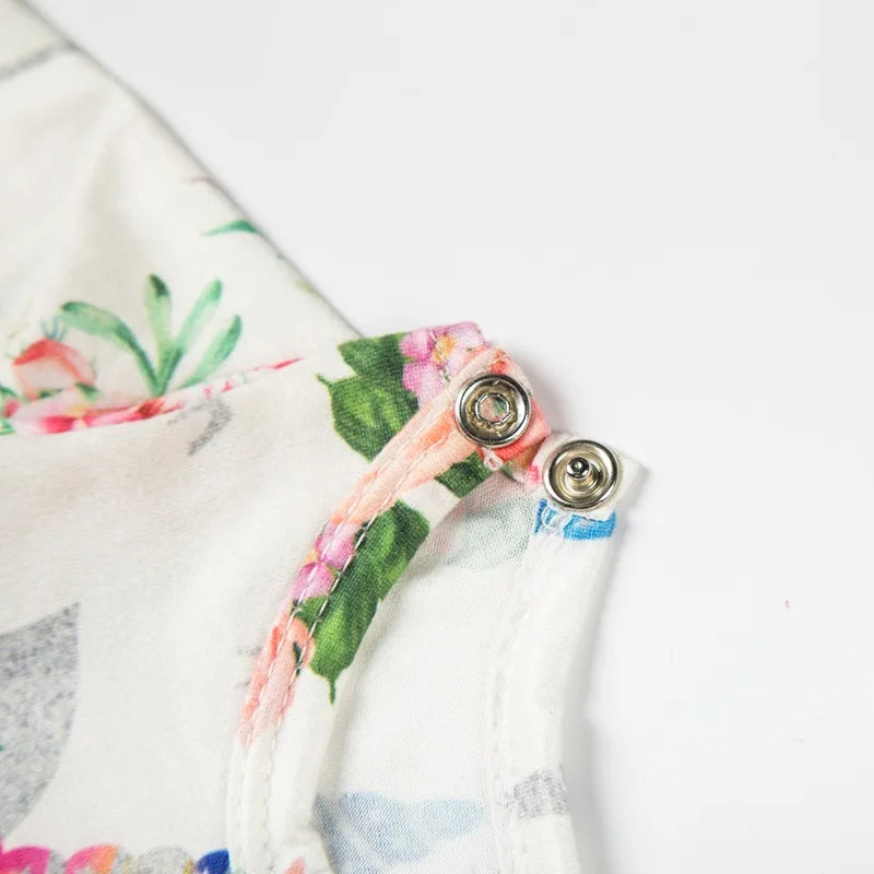 Close-up of a white handmade doll dress featuring floral embroidery and a pink fabric tie detail.