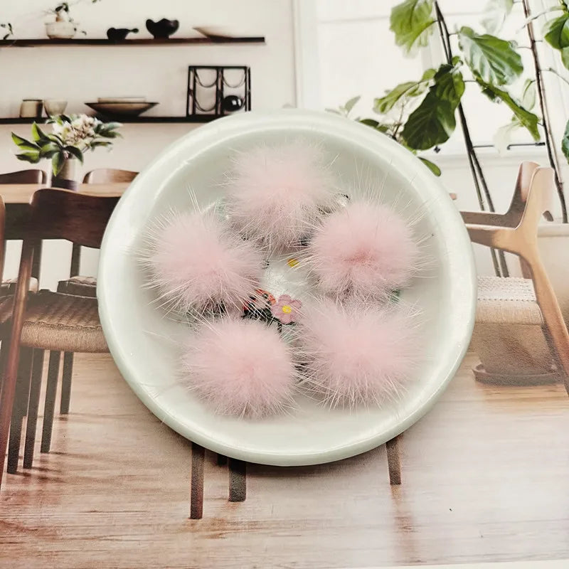 A white bowl filled with pink fluffy mink fur pom poms for crafts and accessories