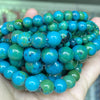 A hand holds a strand of round, variegated blue-green gemstone beads for jewelry making.