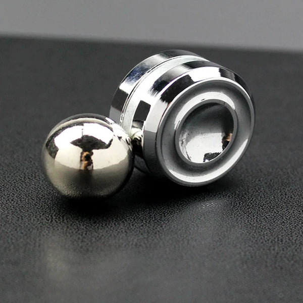 A silver metal desktop fidget spinner with a spherical top resting on a dark surface.