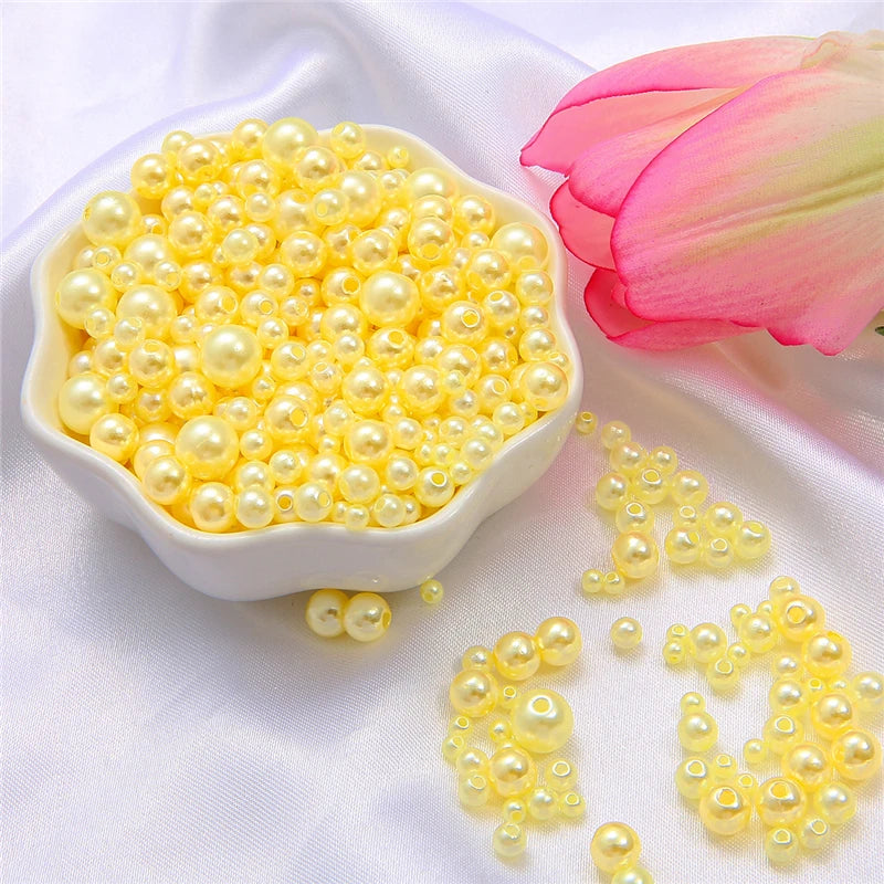 A white dish filled with yellow pearl beads and loose yellow pearl beads on a white satin cloth next to a pink rose.
