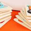 A stack of wooden puzzle pieces shaped like cartoon animals in various colors on an orange surface.