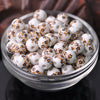 A clear glass bowl filled with small white ceramic beads decorated with orange floral patterns.