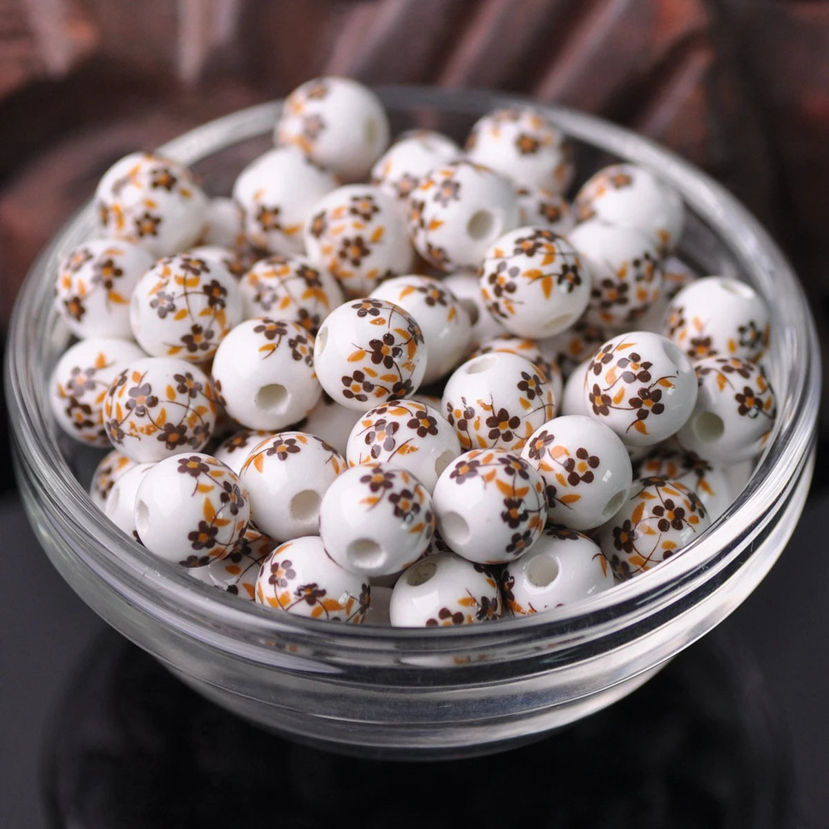 A clear glass bowl filled with small white ceramic beads decorated with orange floral patterns.