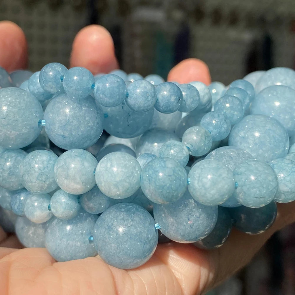 A hand holds a cluster of light blue translucent gemstone beads for jewelry making