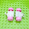 A set of pink and white city traffic vehicle building blocks with trucks and buses placed on a bright green grid surface.