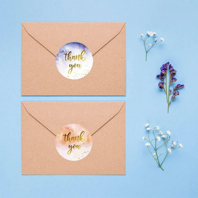 Two kraft paper thank you cards with watercolor designs, one purple and white, the other peach and yellow.