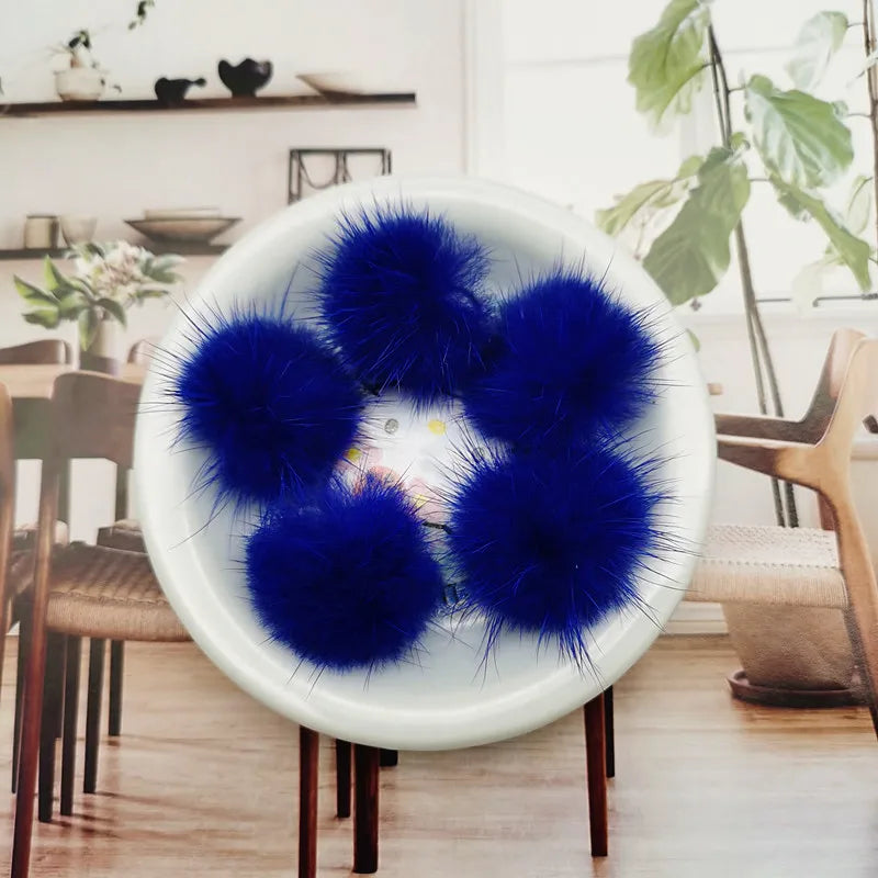 A white bowl filled with bright blue fluffy mink fur pom poms for crafts and accessories.