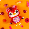 A red and pink animal-themed building block figure resembling a tiger face is displayed on an orange background.