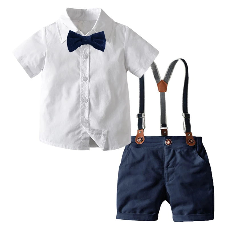 A white dress shirt with a blue bow tie and navy shorts and suspenders for a boy's formal outfit set.