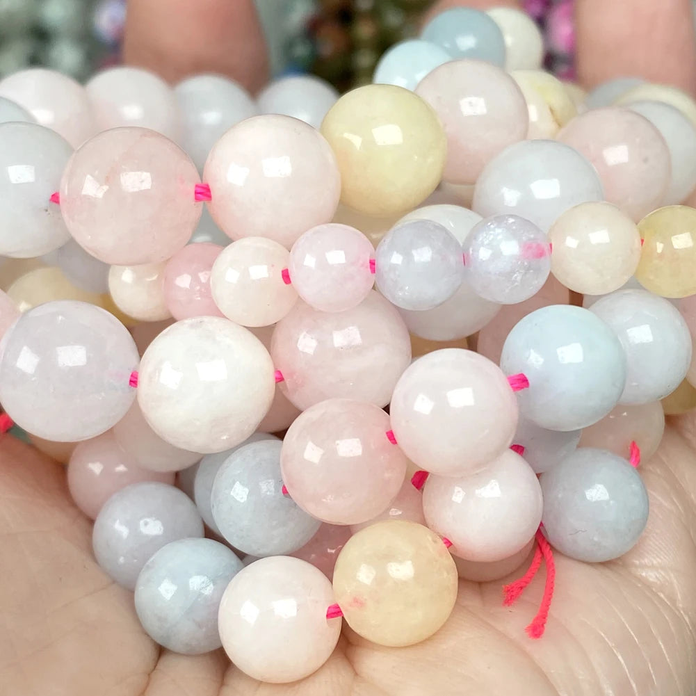 A collection of natural gemstone beads in various shades of pink, white, yellow, and blue are held in a person's hand.