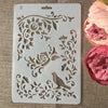 A white flower vine layering stencil with floral and bird designs is shown on a burlap background.
