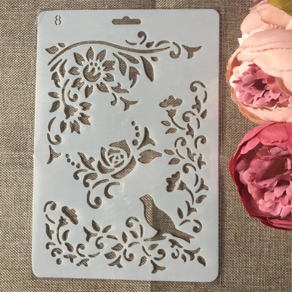 A white flower vine layering stencil with floral and bird designs is shown on a burlap background.