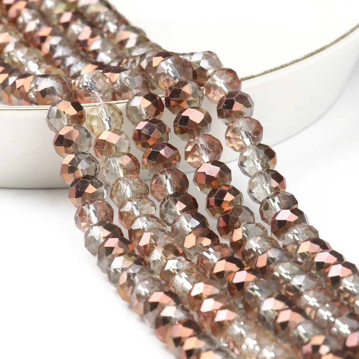 A close-up of faceted crystal glass beads in shades of rose gold and gray, arranged on a white surface.
