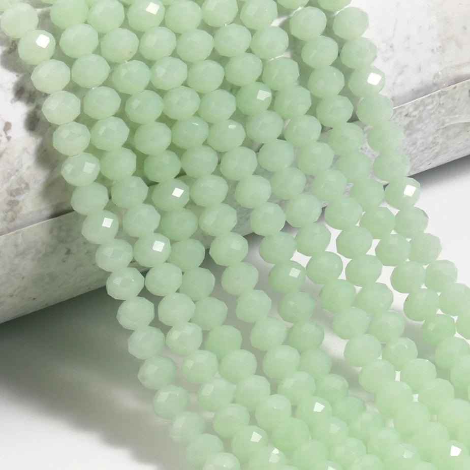 A strand of pale green faceted crystal glass beads laid out on a white surface.