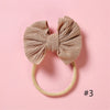A beige fabric bow headband with a soft elastic band is shown against a pink background.