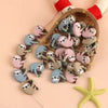 A collection of adorable sloth silicone beads in various shades and poses arranged on a wooden tray.