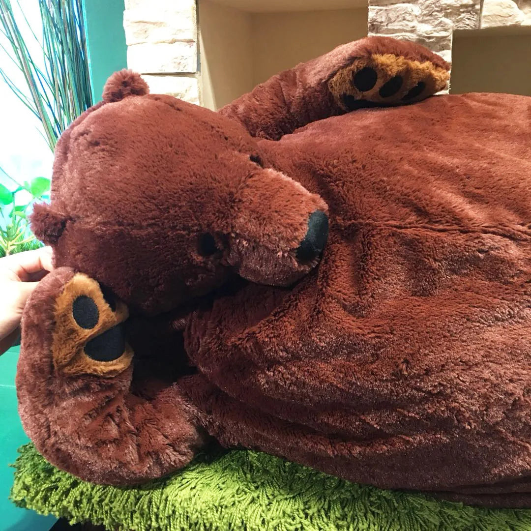 A large, brown, lifelike bear plush cushion resting on a green textured surface.