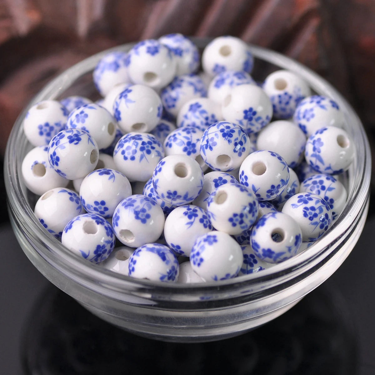 A clear glass bowl filled with small white and blue floral ceramic beads for jewelry making
