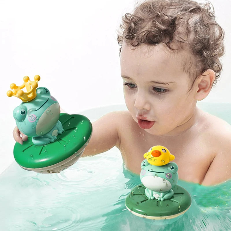 A baby is playing with a floating electric water sprinkler frog bath toy in clear water.