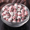 A clear glass bowl filled with small white ceramic beads decorated with red floral patterns.